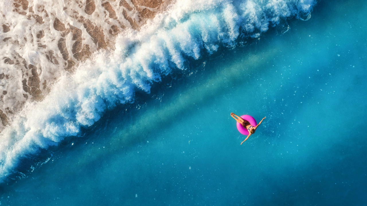 Eine Frau schwimmt auf einem pinken Schwimmring im Meer.