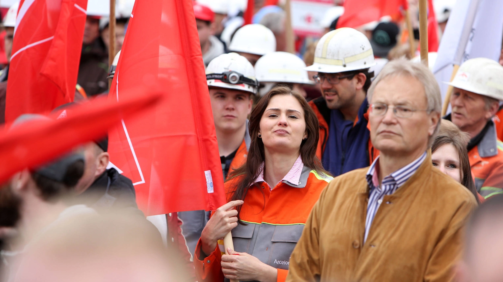 Eine junge Frau mit IG Metall-Fahne blickt entschlossen in die Kamera.