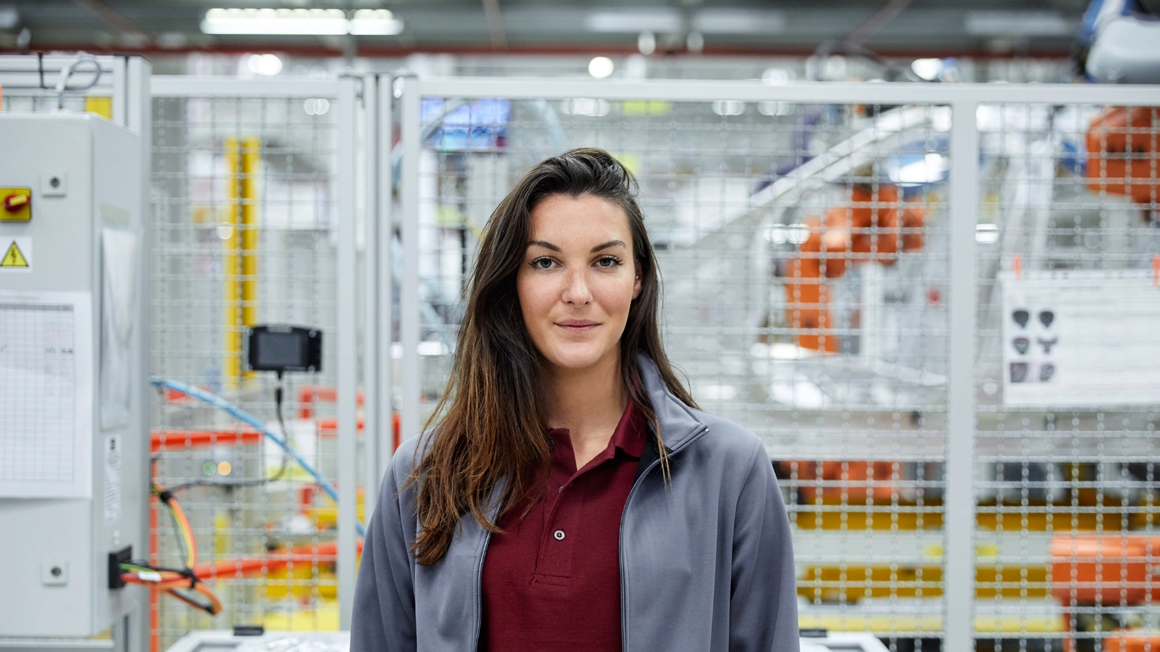 Junge Ingenieurin in der Automobilindustrie steht in der Werkhalle und blickt direkt in die Kamera.