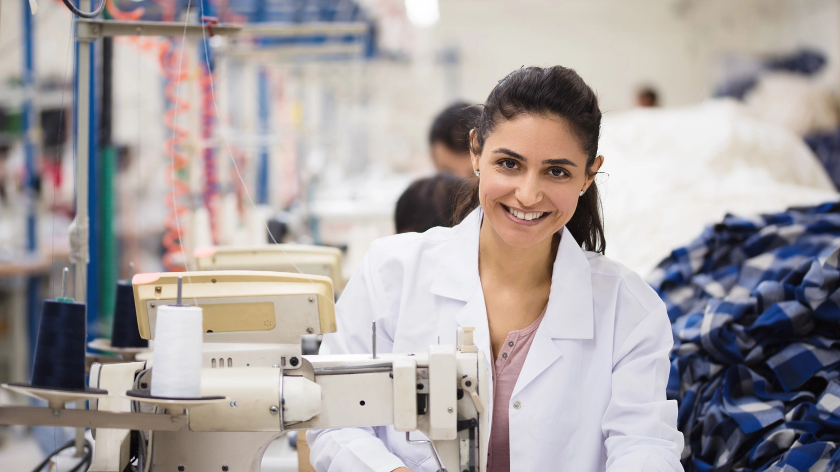Junge Frau sitzt an einer Nähmaschine und lächelt in die Kamera