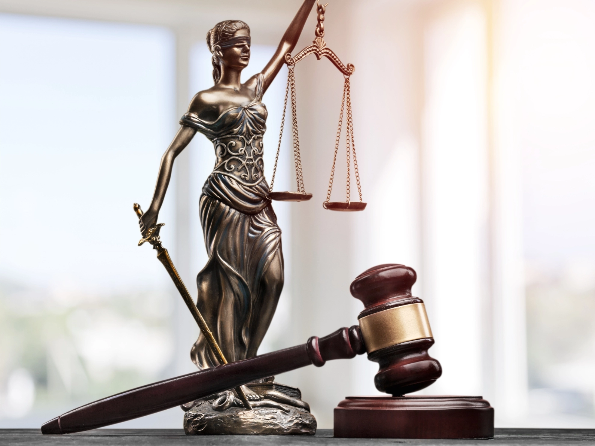 Eine Statue von Justizia liegt neben einem Richterhammer auf einem Tisch