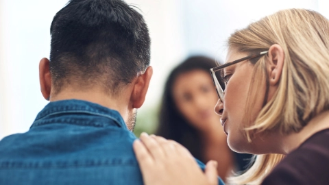 Eine Frau spricht mit einem Mann und legt ihm dabei die Hand auf die Schulter.